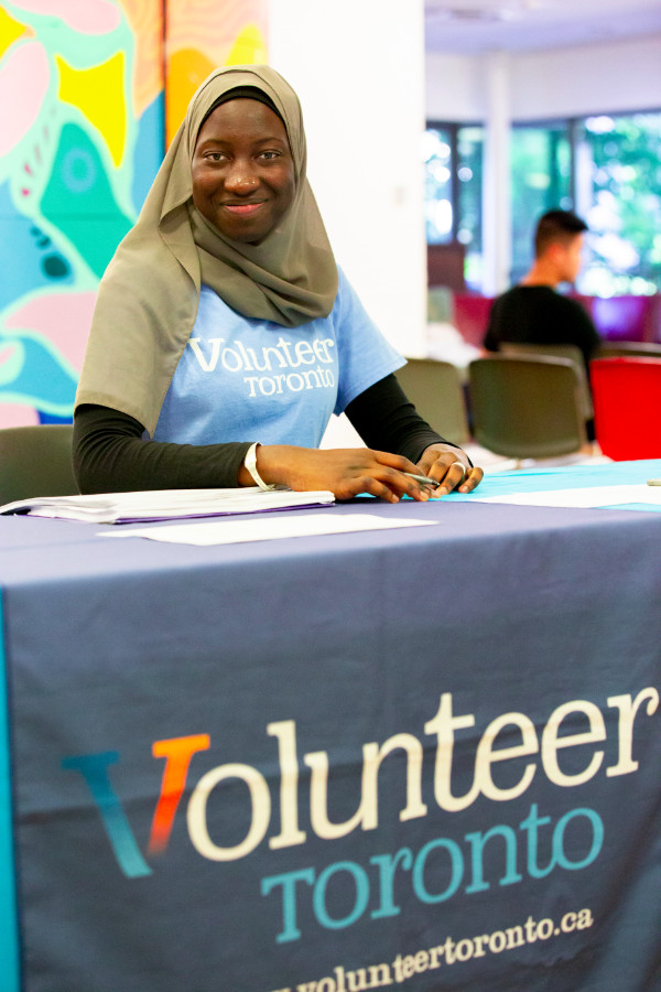 Woman in Volunteer Toronto shirt seated at table with Volunteer Toronto banner
